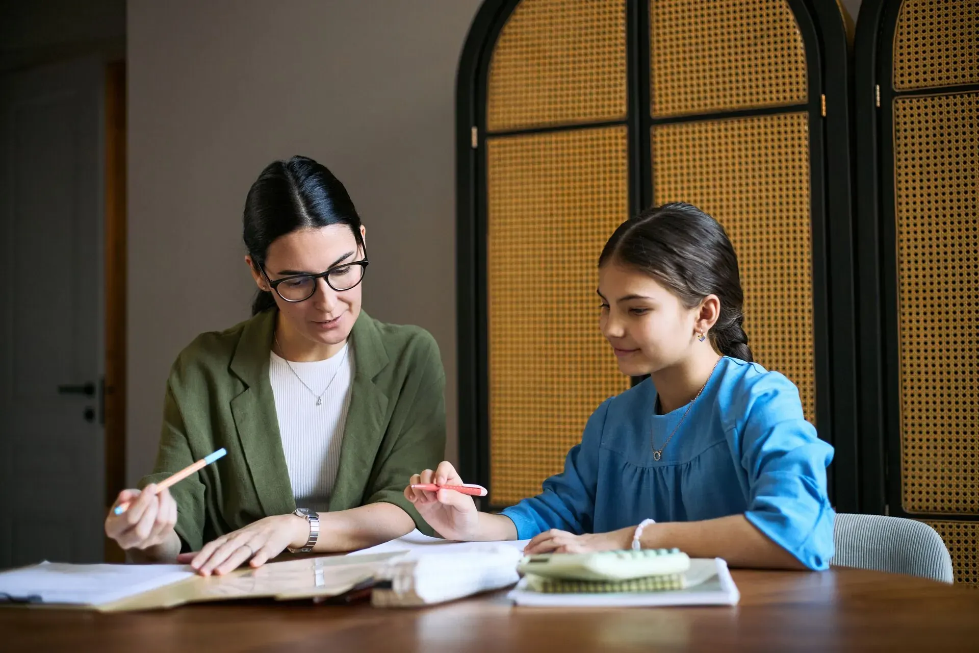 Lehrerin erklärt einer Schülerin am Tisch eine Aufgabe im Heft