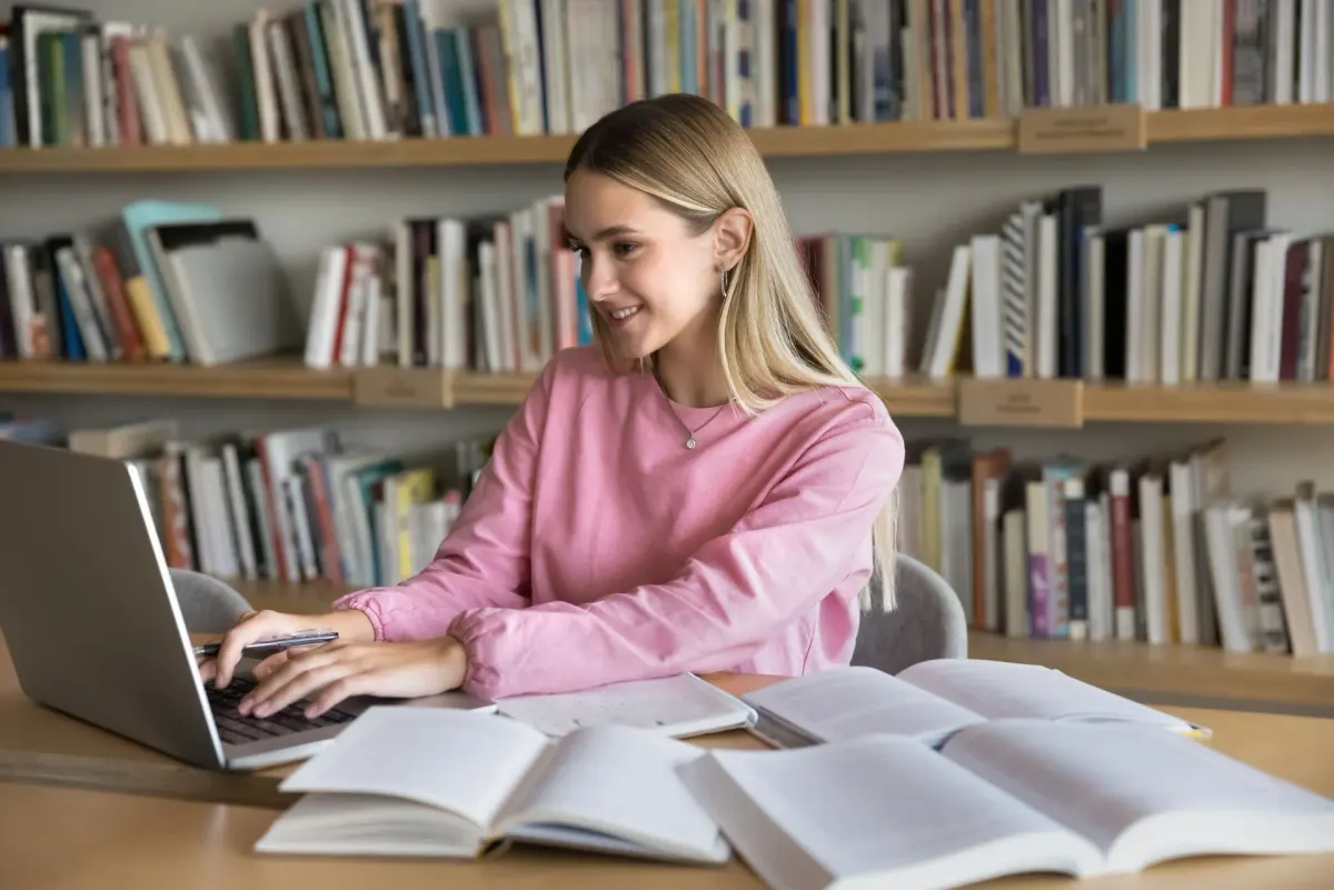 Schülerin lernt in einer Bibliothek mit Laptop und aufgeschlagenen Büchern