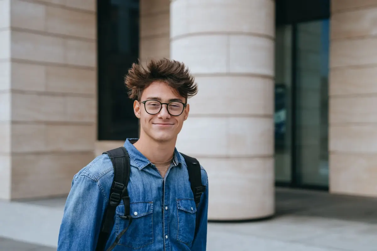 Jugendlicher mit Brille und Rucksack in einer hellen Schulhalle